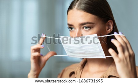 Disease Prevention. Close up beautiful woman putting on mask to prevent virus, holding it by the ear loops, copy space