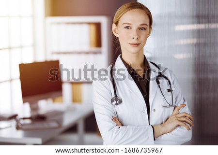 Cheerful smiling female doctor standing with arms crossed in clinic. Portrait of friendly physician woman. Medicine concept
