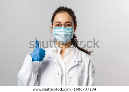 Covid19, coronavirus, healthcare and doctors concept. Portrait of optimistic asian female doctor assure everything be okay, thumb-up, wear medical mask to prevent catching virus, white coat Royalty-Free Stock Photo #1686737194
