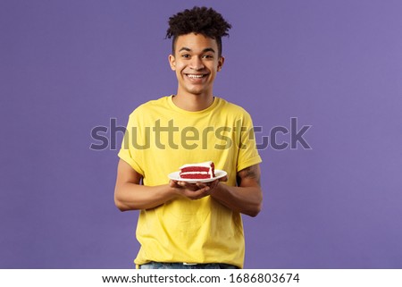 Celebration, party and holidays concept. Portrait of handsome young smiling man, feeling happy likes eating desserts, ordered delivery from local cafe to have some delicious cake, purple background