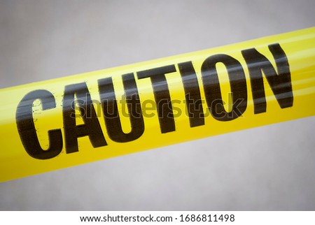 Single word CAUTION in black letters on yellow tape stretched diagonally across the frame in natural light