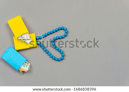 yellow and blue shopping bags with money and blue necklace on grey background
