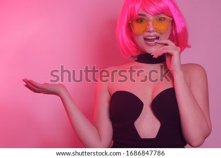 A bright girl on a pink background, in a pink short wig with a bang, holds her hand. A girl advertises your product, free space for text. Anchor photo to advertise your product. Girl shows