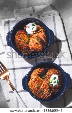 Flat lay of hasselback potatoes in blue pans on a kitchen towel on a gray texture background