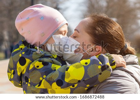 Young mother kisses her daughter through protective medical masks. Covid-19 Coronavirus Pandemic, Virus Protection.