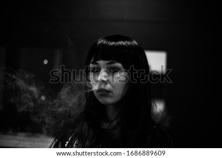 Vaping teenager. Young pretty white caucasian teenage brunette girl with problem skin smoking an electronic cigarette indoors. Life-threatening bad habit. Vape activity. Black and white.