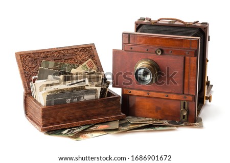 Vintage film photo-camera and old family photos stacked in wooden box isolated on white background.
