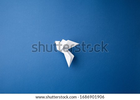 Origami pigeon on a blue isolated background. World Peace Day concept. Close up studio photo.