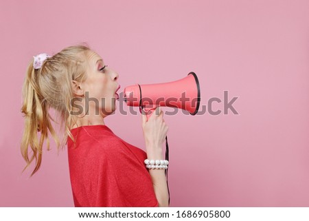 silly young blond woman shouting through a megaphone on pink isolated background
