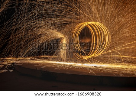 Amazing sparks and flames long exposure steel wool night photography on dark background. A woman, holding umbrella with her hands, trying to protect herself against a man's violence.