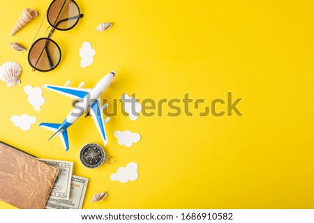 Travel accessories and items on a yellow background with a top view and copy space. Toy airplane in the clouds and a passport, money, glasses. Travel concept background for travel agency banner.