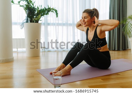 Young fit woman in black sportswear is doing sit-ups at home. Young woman exercising at home due to COVID 19 pandemic. Royalty-Free Stock Photo #1686915745