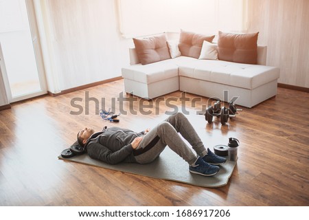 Young ordinary man go in for sport at home. Regular beginner lying on mat on floor and has rest. Real picture of guy with ordinary body. Loosing weight or trying to keep fit