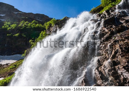 Beautiful scenic landscape of Imeretinskiy waterfall in Caucasus mountains, Karachai-Cherkess Republic. Imeretinka river waterfall at summer in sunlight with splashes and blue sky Royalty-Free Stock Photo #1686922540