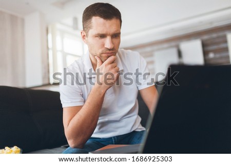 Young man watch tv in his own apartment. Concentrated confident guy watching sport match, game or program. Also watch movie or film. Intension looking at screen