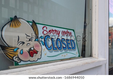 Vintage sorry we're closed sign in a window of a store, restaurant, barber shop, or boutique. The sign is a baby's face crying with tears coming from its eyes with the words sorry we're closed.