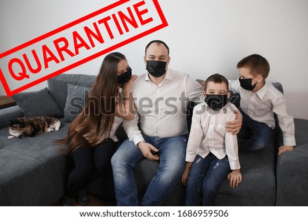 young couple and two children are sitting in a room on a gray sofa in black virus masks, red inscription quarantine, concept of quarantine measures during the period of the disease epidemic