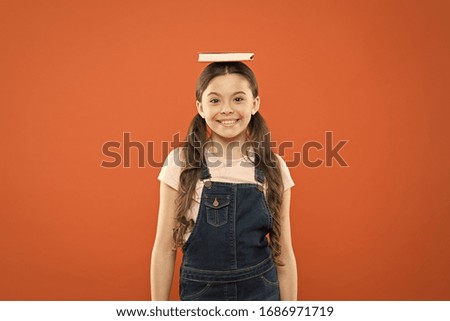 Find balance. Book on her head. Harmony inside. Little girl holding text book head. Small girl book orange background. Interesting story for kid. Studying and relaxing. Motivation and inspiration.