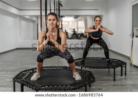 Portrait of two young active girls in fitness clothes doing exercises for  squatting with trampoline during training in gym. Royalty-Free Stock Photo #1686983764