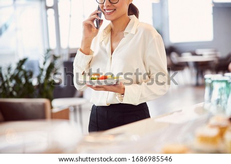 Smiling young woman talking on cellphone and holding plate of salad stock photo
