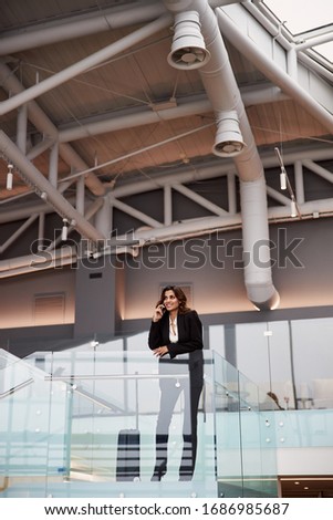 Stylish young woman talking on cellphone at airport waiting area stock photo