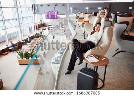 Beautiful lady sitting in chair and stretching while waiting for flight in departure lounge stock photo