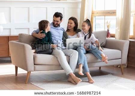 Happy young family enjoying free leisure time with kids siblings, using computer. Smiling married couple communicating with children, watching comedian movie, discussing cartoons in living room.