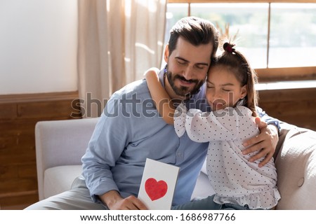 Affectionate young father hugging little child daughter, feeling grateful for birthday congratulations. Thankful daddy holding present, cuddling school aged small kid girl, fathers day celebration.