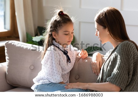 Upset small schoolgirl having trustful conversation with compassionate young mother, sitting together on sofa. Wise mommy comforting soothing little child daughter, overcoming problems at home. Royalty-Free Stock Photo #1686988003