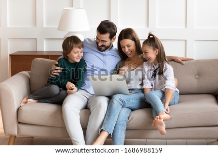 Happy couple cuddling kids siblings, watching comedy movie or funny cartoons on laptop together at home. Excited parents enjoying spending leisure weekend time with small children, sitting on sofa.