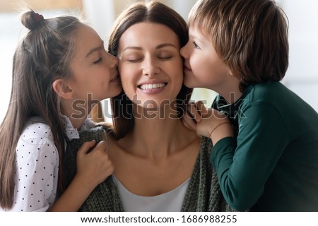 Head shot close up loving little kids siblings kissing cheeks of affectionate young mommy. Smiling mother enjoying tender moment with small daughter son at home, good family relations concept.