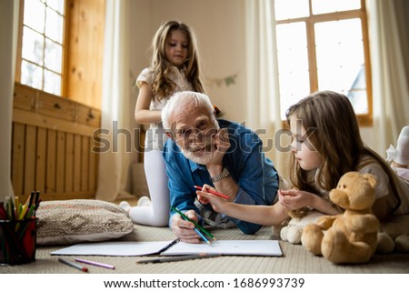 Mirthful aged man lying on the carpet and drawing with grandchildren. Domestic concept