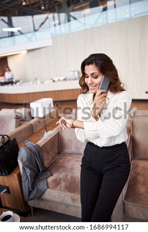 Beautiful young woman having phone conversation and checking time on wristwatch stock photo