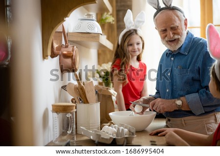 Cute girls wearing bunny ears in the kitchen watching their grandfather cracking eggs into the bowl