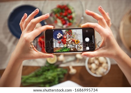 Woman take a picture of different beautiful vegetables and greens with a mobile phone at her kitchen. Smartphone food photography. Healthy eating, vegetarian food, dieting . for weight loss and detox.