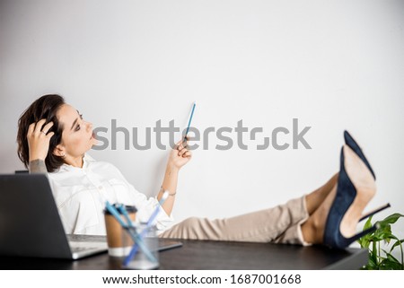 Beautiful young lady sitting at work desk while looking at wall stock photo. Copy space