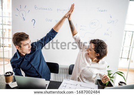 Happy young man and woman working with new project while having good news stock photo. Coworking team meeting