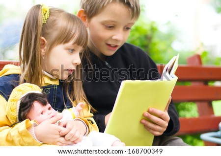 Lovely children - brother and sister, reading a book at the park