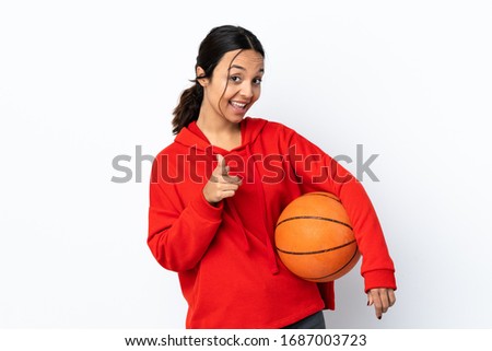 Young woman playing basketball over isolated white background surprised and pointing front