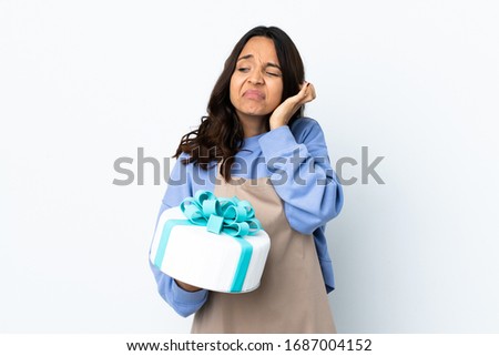 Pastry chef holding a big cake over isolated white background frustrated and covering ears