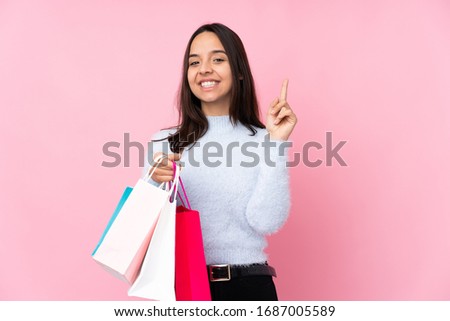 Young woman with shopping bag over isolated pink background showing and lifting a finger in sign of the best