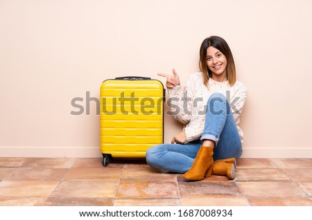Traveler woman with suitcase sitting on the floor pointing finger to the side