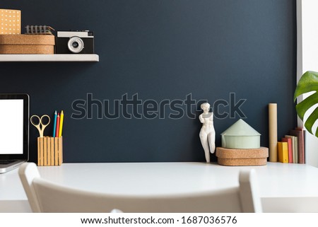 Home office with laptop, stationery, camera, figurine, books around and navy blue wall, Homeschooling concept. Trendy, creative workspace.