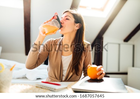 Woman in home office drinking orange flavored amino acid vitamin powder.Keto supplement.After exercise liquid meal.Weight loss fitness nutrition diet.Immune system support.Organic citrus fruit Royalty-Free Stock Photo #1687057645