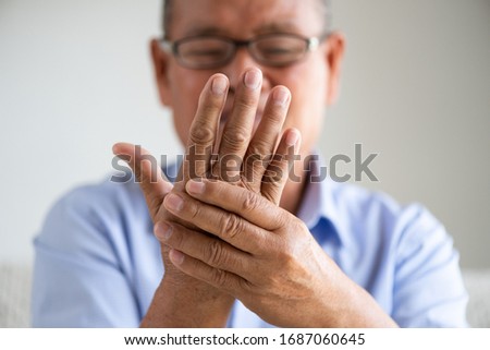 Asian old man sitting on sofa and having hand pain, hand injury at home. Senior healthcare concept.