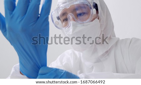 Asian doctor in protective hazmat PPE suit wearing medical latex gloves Royalty-Free Stock Photo #1687066492