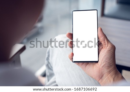 Mockup image of man hand holding mobile smart phone with blank screen, relax sitting in coffee shop, close up, over shoulder view