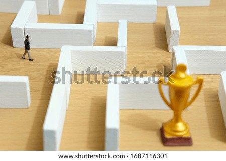 Business strategy conceptual photo - Miniature of businessman on a labyrinth maze seeking the golden trophy