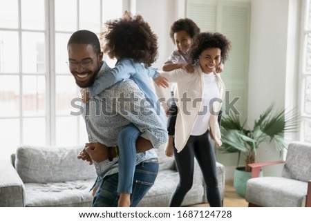 Cheerful African couple play with children running piggy back riding little kids celebrating moving day at new first modern home. Family have fun enjoy free time together leisure active games concept Royalty-Free Stock Photo #1687124728