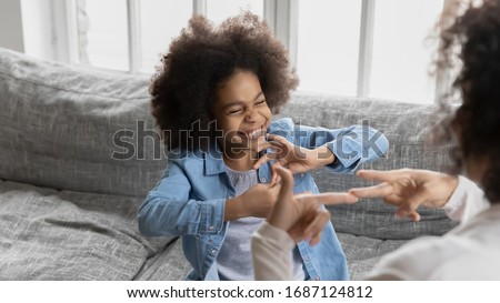 African deaf kid girl and her mother sitting on couch showing symbols with hands using visual-manual gestures enjoy communication at home. Hearing loss disability sign language learning school concept